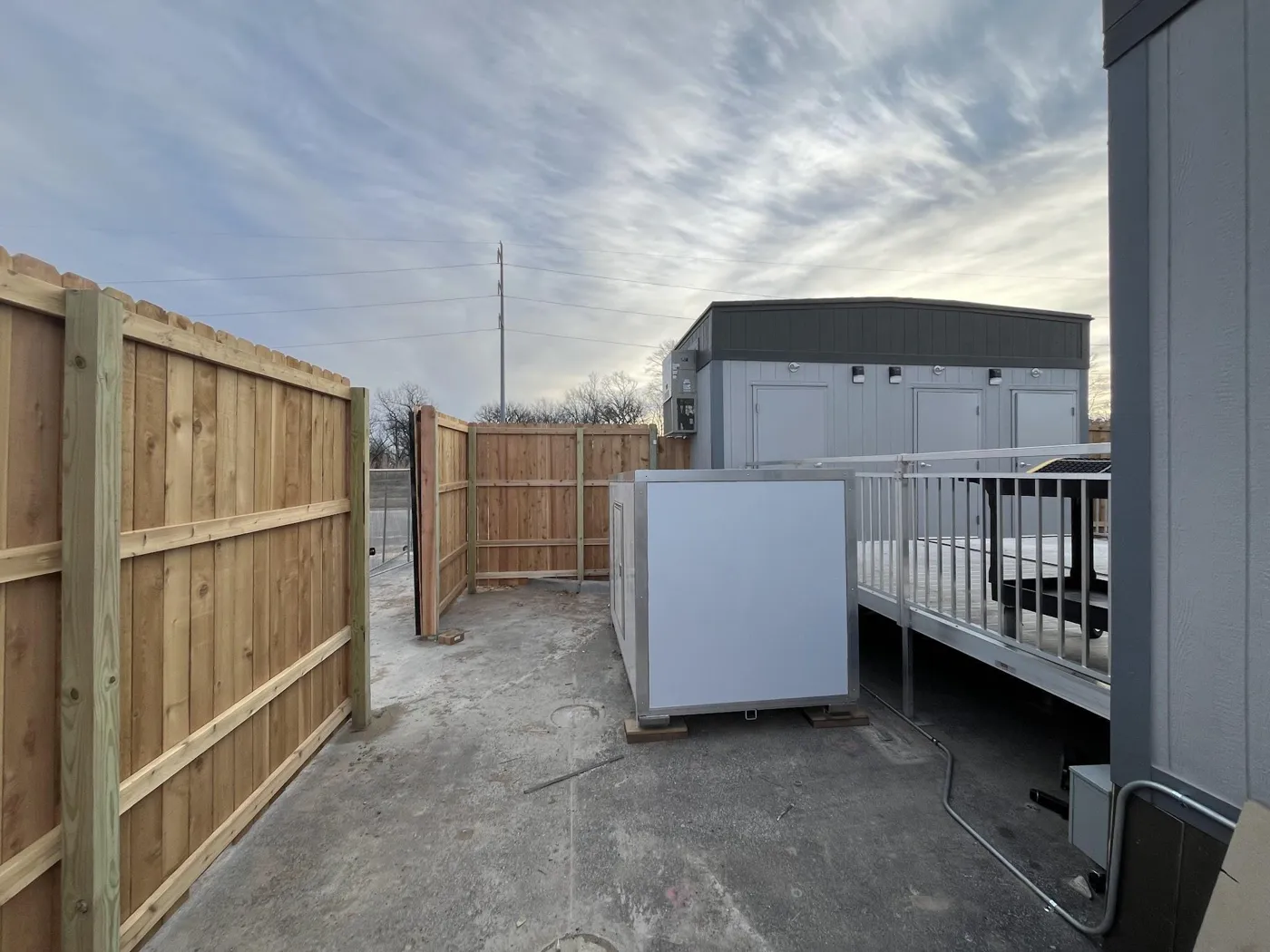Water and waste box installed beside a modular office building next to the entry ramp, screened by a cedar fence